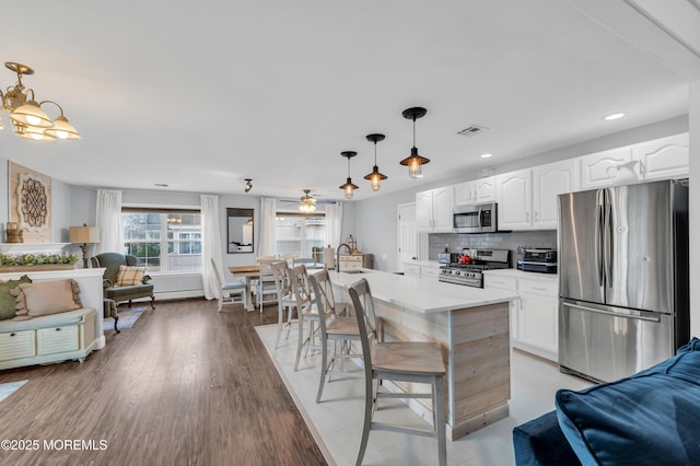 kitchen with a kitchen island, appliances with stainless steel finishes, pendant lighting, white cabinetry, and backsplash