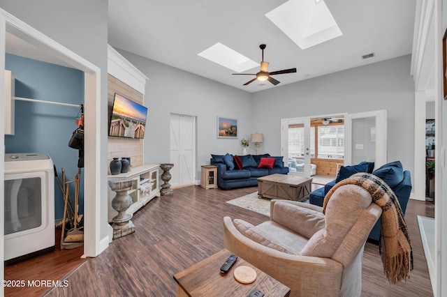 living room featuring dark hardwood / wood-style floors, ceiling fan, washer / clothes dryer, and vaulted ceiling with skylight