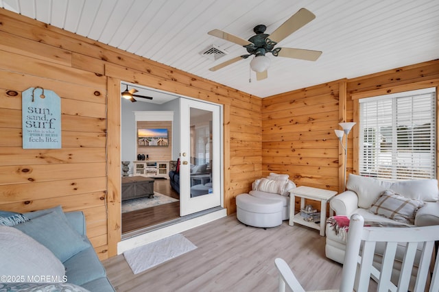 living room with ceiling fan, wooden walls, and light hardwood / wood-style floors