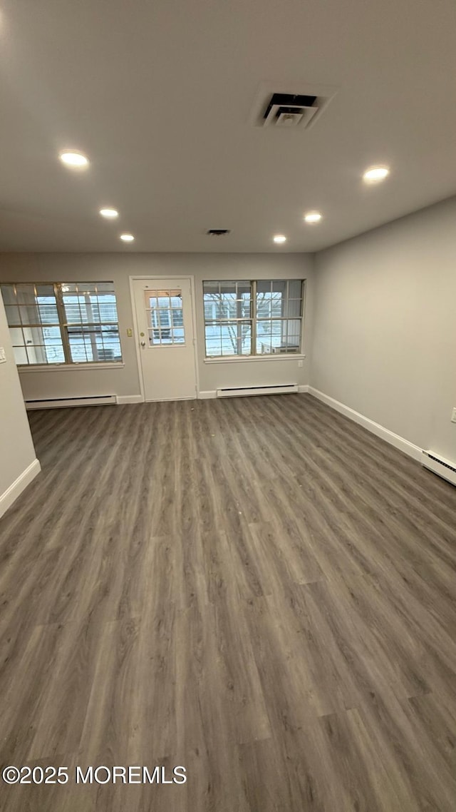 unfurnished living room with plenty of natural light, dark hardwood / wood-style flooring, and a baseboard heating unit