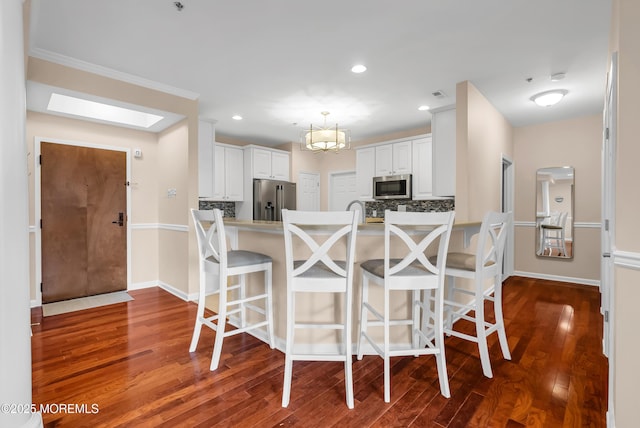 kitchen featuring appliances with stainless steel finishes, hardwood / wood-style floors, white cabinets, backsplash, and kitchen peninsula