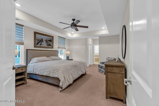 carpeted bedroom with white refrigerator, a raised ceiling, connected bathroom, and ceiling fan