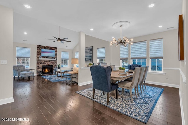 dining area featuring a healthy amount of sunlight, dark hardwood / wood-style floors, vaulted ceiling, and a stone fireplace