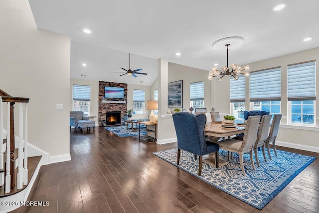 dining room with a fireplace, ceiling fan with notable chandelier, vaulted ceiling, and dark hardwood / wood-style floors