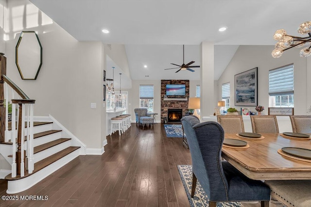 dining space featuring vaulted ceiling, a stone fireplace, dark hardwood / wood-style floors, and ceiling fan with notable chandelier