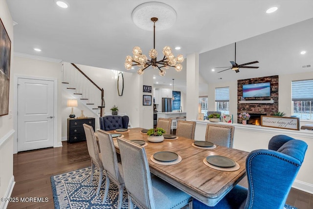 dining space with lofted ceiling, dark hardwood / wood-style floors, ceiling fan with notable chandelier, and a fireplace