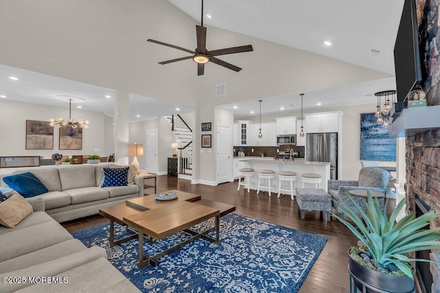 living room featuring ceiling fan with notable chandelier, dark hardwood / wood-style floors, high vaulted ceiling, and a brick fireplace