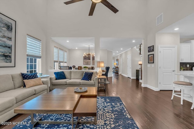 living room with dark wood-type flooring, ceiling fan with notable chandelier, and a towering ceiling