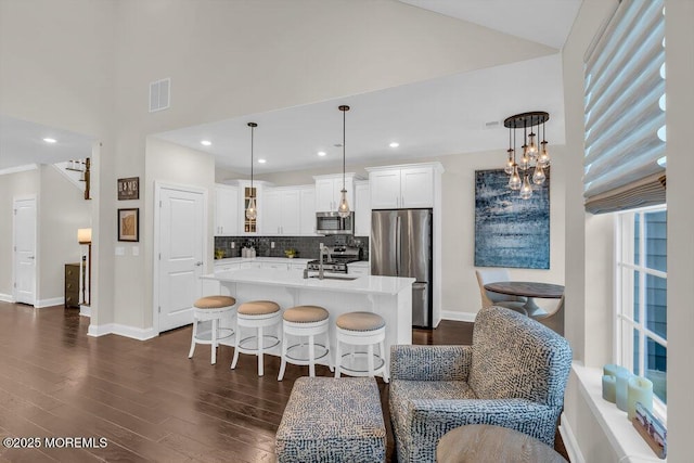 kitchen with white cabinetry, appliances with stainless steel finishes, an island with sink, pendant lighting, and backsplash