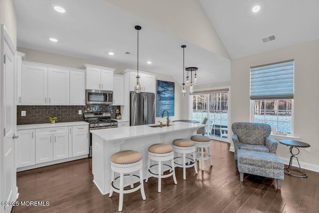 kitchen with appliances with stainless steel finishes, pendant lighting, an island with sink, sink, and white cabinets