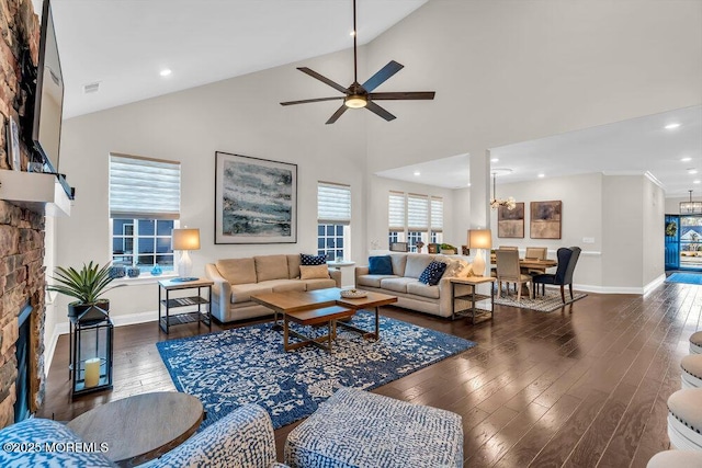 living room with ceiling fan with notable chandelier, a fireplace, high vaulted ceiling, and dark hardwood / wood-style floors