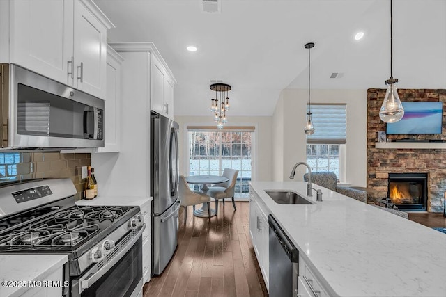 kitchen with white cabinetry, sink, hanging light fixtures, light stone counters, and stainless steel appliances