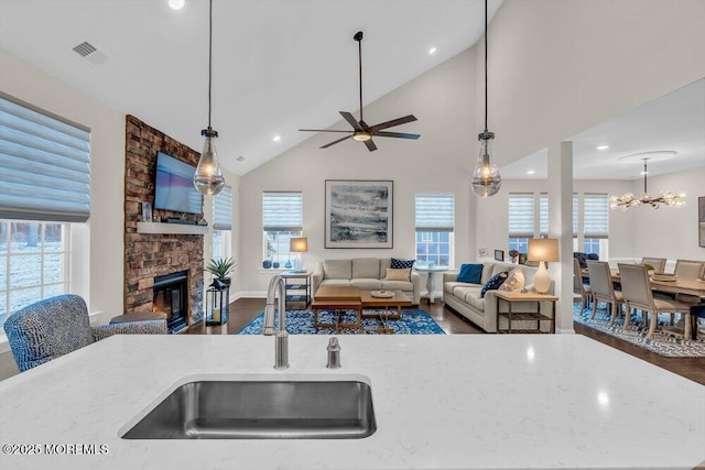 kitchen featuring pendant lighting, a fireplace, sink, a kitchen island with sink, and light stone counters