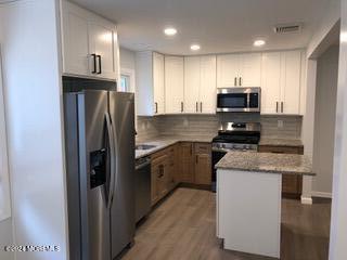 kitchen with white cabinetry, stainless steel appliances, wood-type flooring, light stone countertops, and a kitchen island