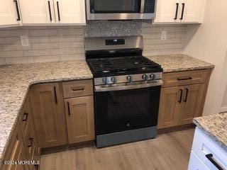 kitchen with backsplash, stainless steel appliances, light stone countertops, and white cabinets