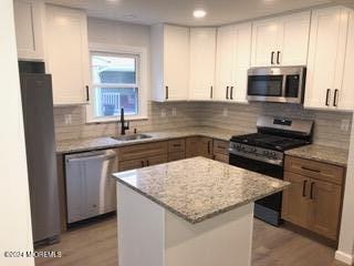 kitchen featuring light wood-type flooring, a kitchen island, stainless steel appliances, light stone countertops, and white cabinets