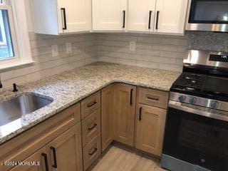 kitchen featuring sink, appliances with stainless steel finishes, white cabinetry, tasteful backsplash, and light stone countertops