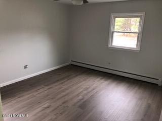 empty room featuring ceiling fan, dark hardwood / wood-style floors, and a baseboard heating unit