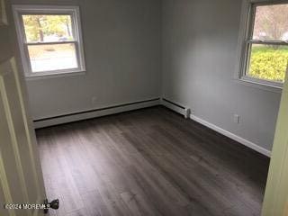 spare room featuring plenty of natural light, a baseboard heating unit, and dark hardwood / wood-style flooring