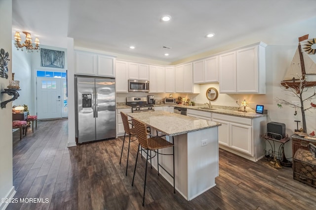 kitchen featuring dark wood-type flooring, appliances with stainless steel finishes, a center island, light stone countertops, and white cabinets