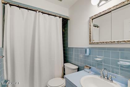 bathroom with vanity, toilet, curtained shower, and tile walls