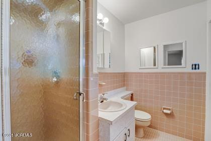 bathroom featuring tile walls, vanity, a shower with shower door, and toilet