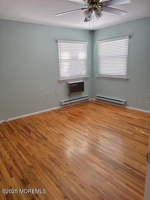 unfurnished room with a baseboard radiator, an AC wall unit, wood-type flooring, and ceiling fan