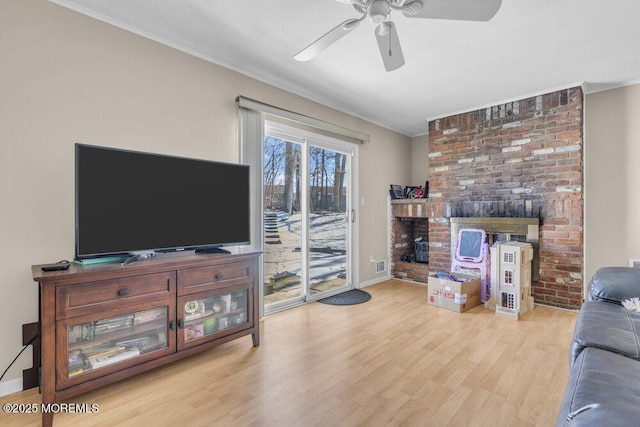 living room featuring ceiling fan, a brick fireplace, ornamental molding, and light wood-type flooring