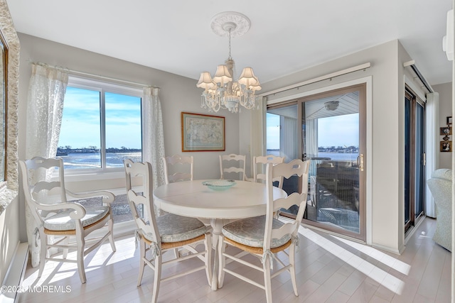 dining room featuring light wood-type flooring, a chandelier, and a water view