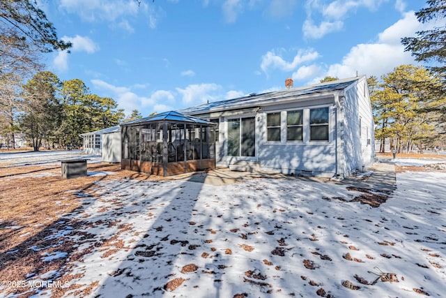 snow covered rear of property with a sunroom