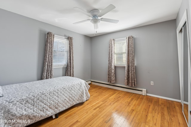 bedroom with hardwood / wood-style flooring, ceiling fan, a closet, and a baseboard heating unit