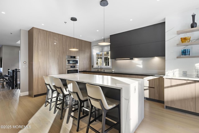 kitchen featuring sink, light hardwood / wood-style flooring, double oven, a kitchen island, and decorative light fixtures