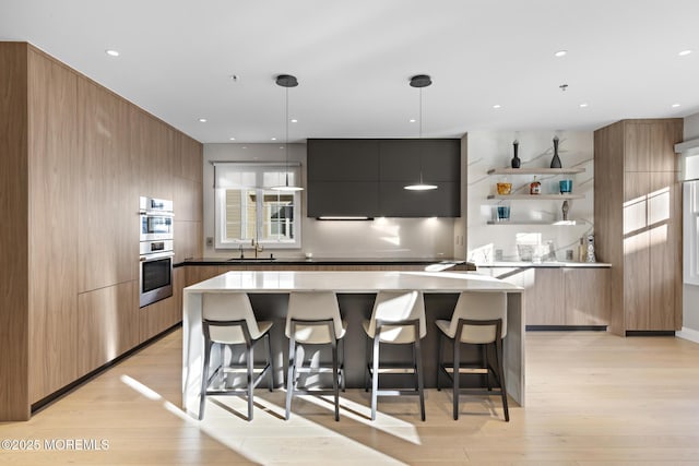 kitchen with pendant lighting, sink, a kitchen breakfast bar, a center island, and light hardwood / wood-style floors