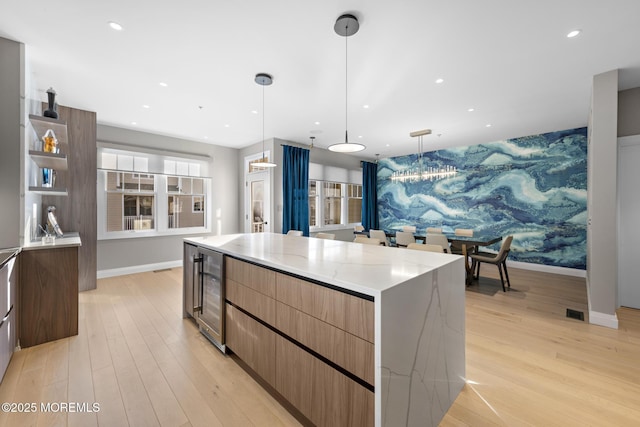 kitchen featuring light stone countertops, pendant lighting, beverage cooler, and a spacious island