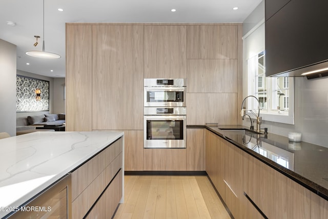 kitchen featuring decorative light fixtures, light stone countertops, double oven, and light brown cabinets