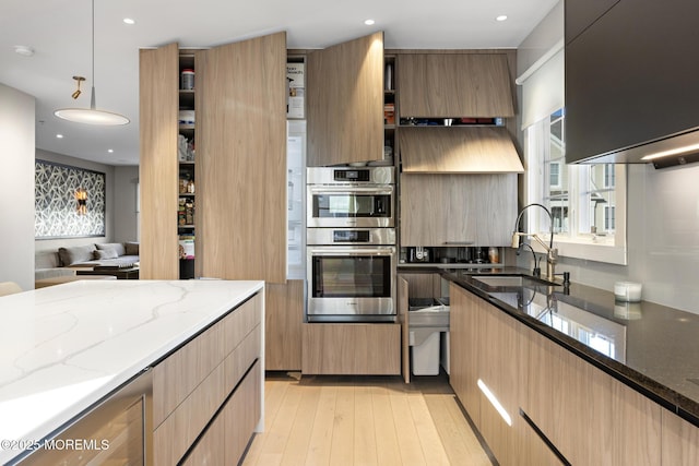 kitchen featuring pendant lighting, sink, dark stone countertops, double oven, and light wood-type flooring