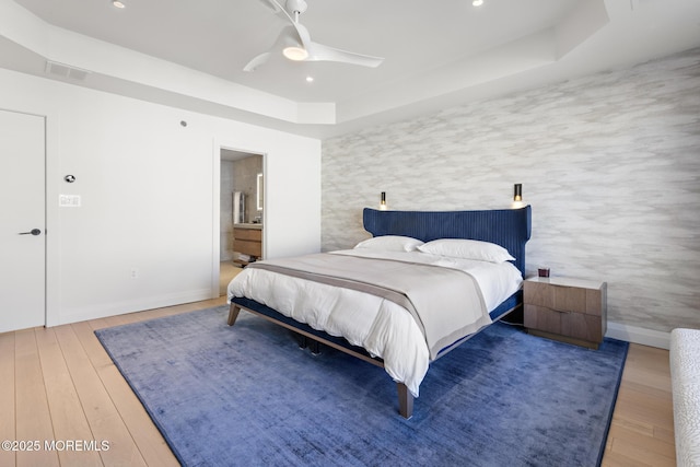 bedroom featuring a raised ceiling, wood-type flooring, connected bathroom, and ceiling fan