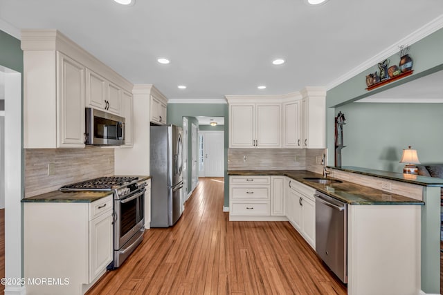 kitchen featuring appliances with stainless steel finishes, sink, white cabinets, ornamental molding, and light wood-type flooring