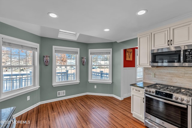 kitchen with appliances with stainless steel finishes, white cabinetry, a skylight, decorative backsplash, and light wood-type flooring