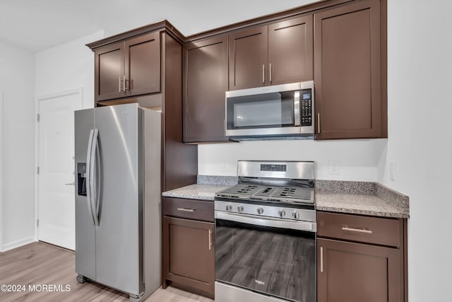 kitchen with light stone counters, appliances with stainless steel finishes, dark brown cabinets, and light wood-type flooring