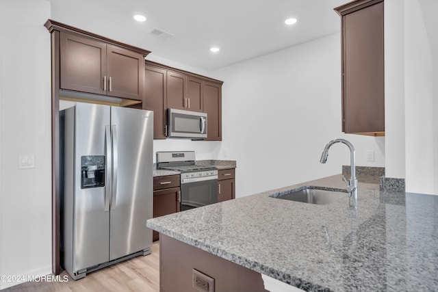 kitchen featuring sink, light stone counters, kitchen peninsula, stainless steel appliances, and dark brown cabinets