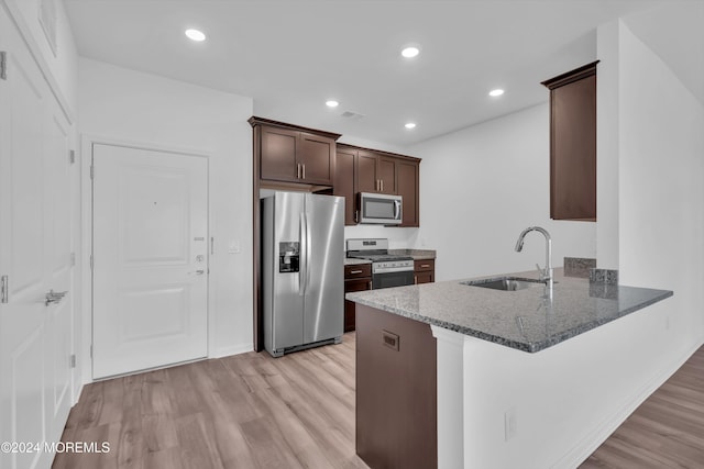 kitchen with dark brown cabinetry, sink, light hardwood / wood-style flooring, appliances with stainless steel finishes, and dark stone counters