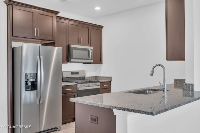 kitchen with dark brown cabinetry, sink, appliances with stainless steel finishes, kitchen peninsula, and stone counters