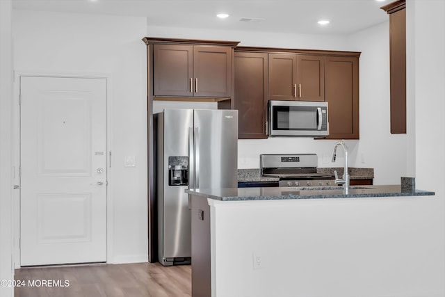 kitchen with appliances with stainless steel finishes, sink, dark stone countertops, kitchen peninsula, and light wood-type flooring