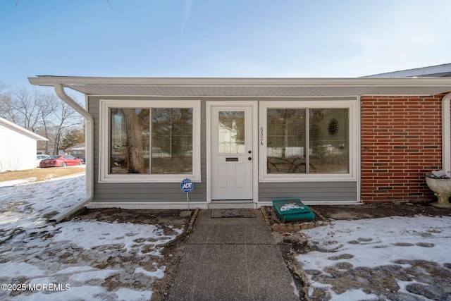 snow covered property entrance featuring brick siding