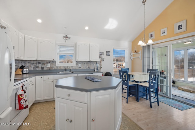 kitchen with lofted ceiling, sink, white cabinets, hanging light fixtures, and white appliances