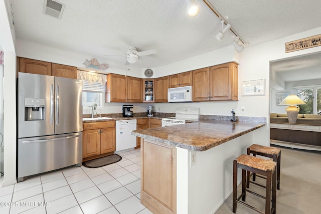 kitchen featuring sink, white appliances, a kitchen breakfast bar, a textured ceiling, and kitchen peninsula