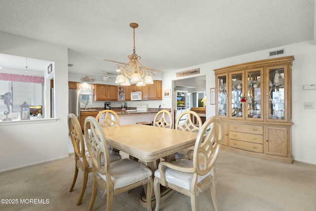 carpeted dining room with sink, a chandelier, and a textured ceiling