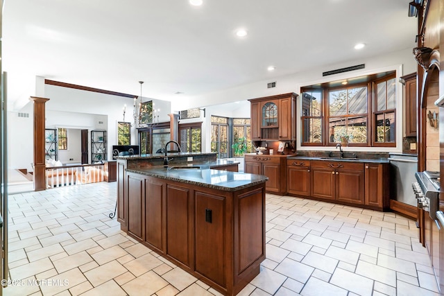 kitchen featuring dark stone counters, sink, decorative light fixtures, and an island with sink