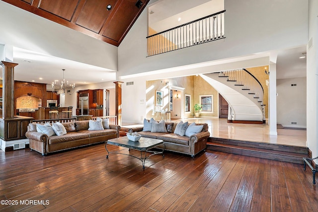 living room with decorative columns, dark wood-type flooring, and an inviting chandelier